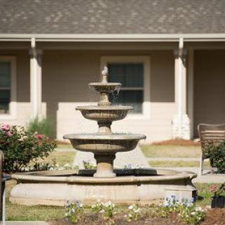 A three-tiered stone fountain in front of a building, surrounded by a garden.