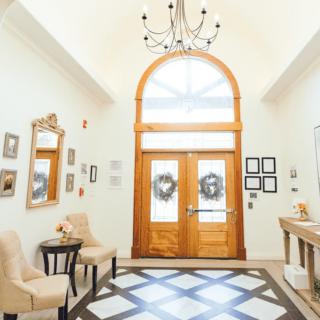 A beautifully decorated foyer with a grand wooden front door, a chandelier, and elegant furnishings.