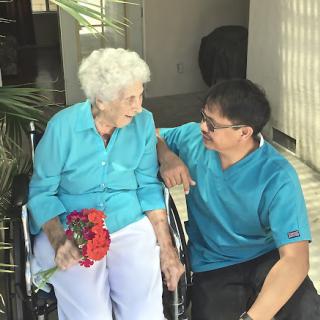 A warm moment shared between an elderly woman in a wheelchair and a man, as they engage in a heartfelt conversation with flowers in hand.