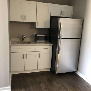 A compact kitchen area with white cabinets, a refrigerator, microwave, and sink.