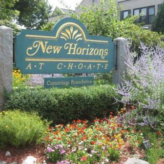 Entrance sign for New Horizons surrounded by lush landscaping and colorful flowers.