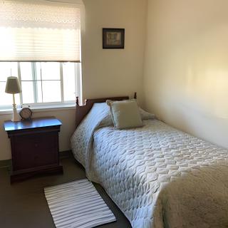 A cozy, minimalist bedroom with a single bed and a nightstand next to a window.