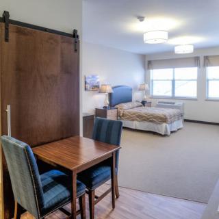 A spacious hotel room with a bed, table and chairs, featuring ample lighting and large windows.