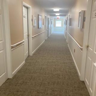 A long indoor hallway with carpeted flooring and multiple doors along both sides.