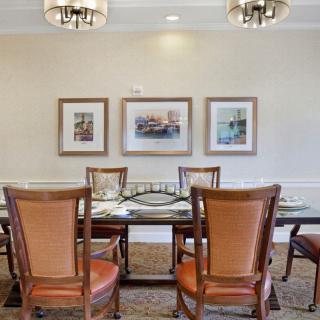 A neatly arranged dining room with a glass table, surrounded by wooden chairs and adorned with framed art on the walls.