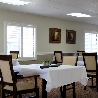 A neatly arranged dining room with tables and chairs, accompanied by paintings on the wall and large windows.