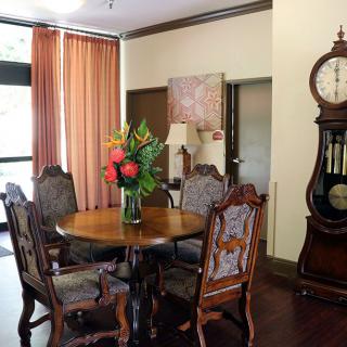 A cozy dining room with antique furniture, featuring a round wooden table surrounded by ornate chairs and decorated with a vase of vibrant flowers.