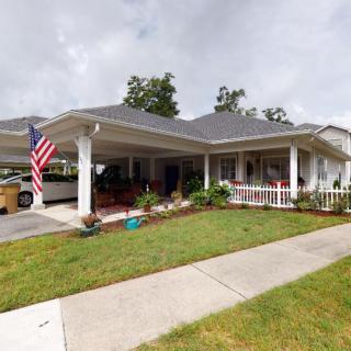 A suburban house with a porch and well-maintained lawn, featuring a flag displayed near the driveway.