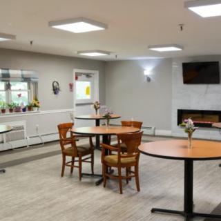 A modern dining space featuring round tables, wooden chairs, and a TV mounted above a fireplace.