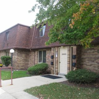 A two-story residential building with a brick exterior, surrounded by greenery and a sidewalk.