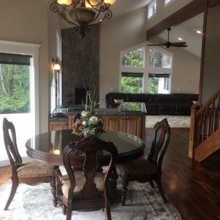 A modern dining room with a wooden table and chairs, adjacent to a living area with large windows.