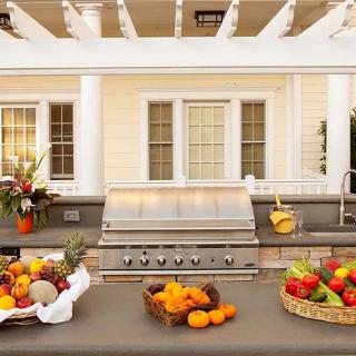 A beautifully arranged outdoor kitchen with a grill and baskets of fresh fruits, perfect for summer entertaining.