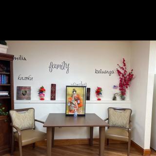 A cozy office space featuring two chairs, a table with artwork, decorative flowers, and a bookshelf.