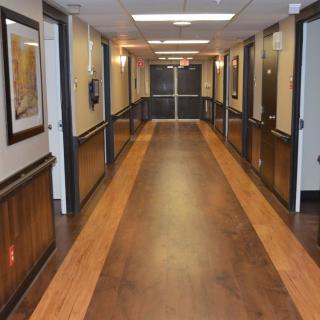 An empty hallway with polished wooden floors and bright lighting, featuring multiple doors on both sides.