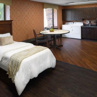 A cozy studio apartment featuring a single bed, dining table, kitchenette, and laundry appliances.