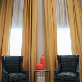 Two armchairs with a side table and decorative vases in front of large yellow curtains.