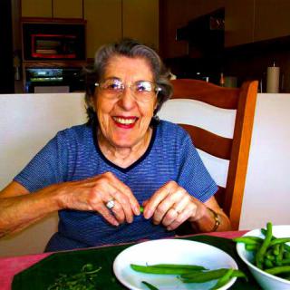 An elderly woman smiles while sitting at a dining table with vegetables.