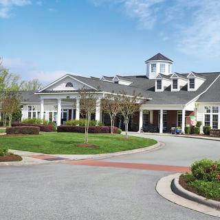 A large residential building with a circular driveway and landscaped surroundings under a clear blue sky.