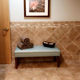 A small bench in a tiled room with folded towels and artwork on the wall.