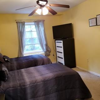 A cozy bedroom with twin beds and a ceiling fan, featuring yellow walls and a window with curtains.