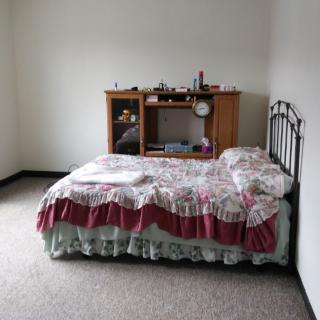 A simple bedroom with a neatly made bed and a small wooden desk.