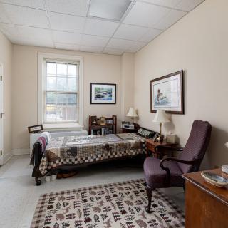 A cozy bedroom with a patterned bedspread, two chairs, and framed artwork on the walls.