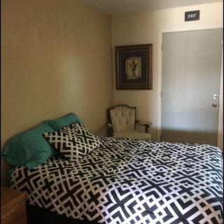 A cozy bedroom with a patterned bedspread, chair, and wall art.