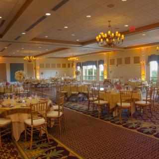 A spacious banquet hall set up with tables and chairs, elegantly decorated and illuminated by chandeliers.