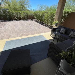 A cozy patio area featuring comfortable seating, surrounded by greenery under a bright sky.