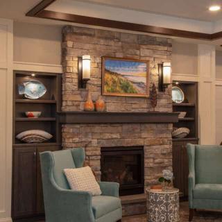 A cozy living room with a brick fireplace, decorated with artwork and flanked by built-in shelves and armchairs.