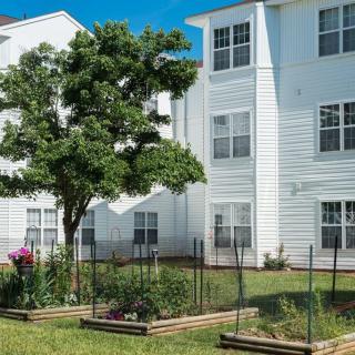 A residential apartment building with a fenced garden and trees in the foreground.