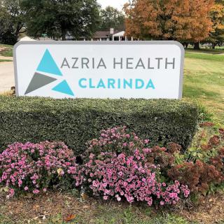 Signage for Azria Health in Clarinda, surrounded by flowers.