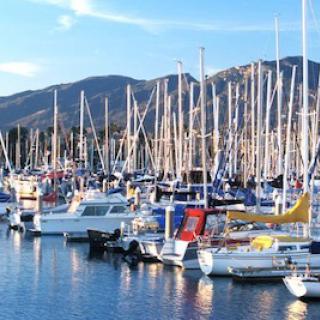 A bustling marina filled with sailboats against a backdrop of mountains and a clear blue sky.