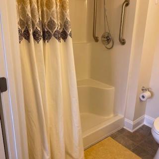 A bathroom with a shower featuring grab bars and a patterned curtain.