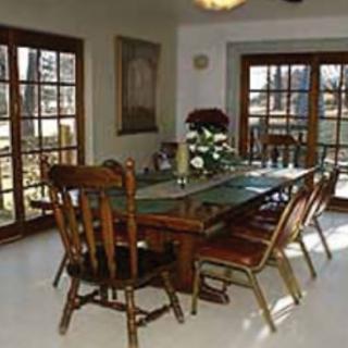 A brightly lit dining room with a wooden table and chairs, surrounded by large windows.