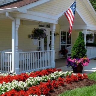 A charming house with a porch and an American flag, surrounded by beautifully arranged flowers in the garden.