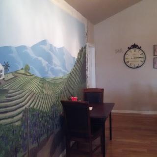 A dining room with a mural of mountains and rice terraces on the wall, featuring a small table with two chairs and a clock hanging above.