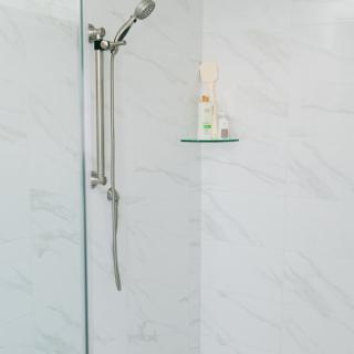 A minimalist, modern shower with marble walls and a single shelf.