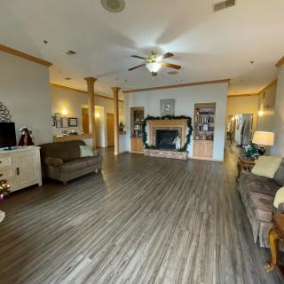 A spacious living room with wood flooring, featuring a fireplace, seating area, ceiling fan, and built-in bookshelves.