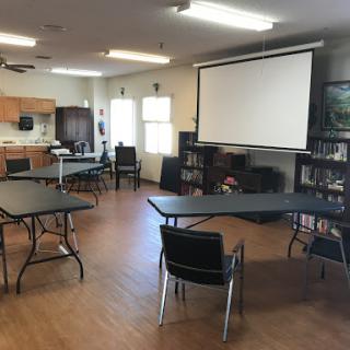 A meeting room equipped with tables, chairs, and a projector screen.
