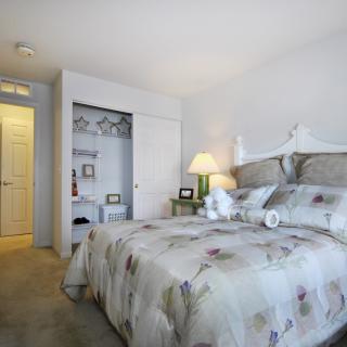 A cozy bedroom featuring a neatly made bed with floral bedding, a bedside lamp, and an open closet.