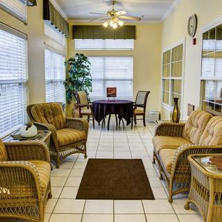 A cozy living room with wicker furniture, a small round table, and large windows.