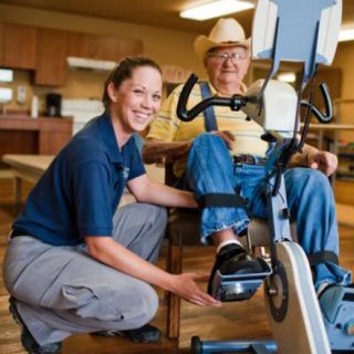 A healthcare professional assists a senior citizen with exercise equipment in a rehabilitation setting.