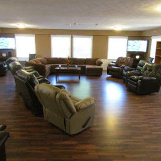 A spacious living room with multiple sofas and recliners arranged in a circle on wooden flooring.