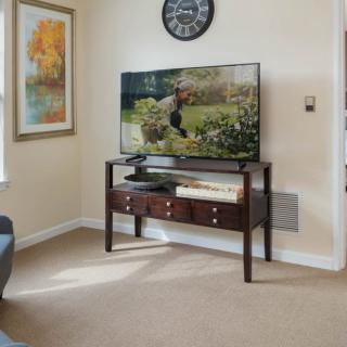A cozy living room featuring a television on a console table, decorated with a wall clock and artwork.