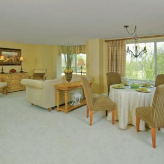 A spacious living and dining area with soft neutral tones, featuring comfortable furniture and large windows letting in natural light.