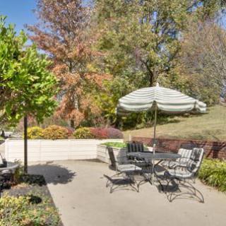 A serene outdoor patio area with a table, chairs, and umbrella surrounded by lush greenery and trees.