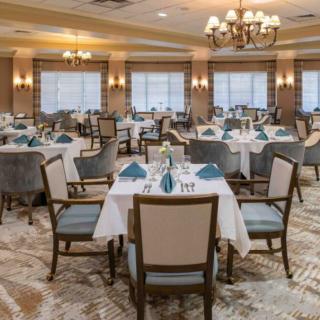 An elegant dining room with neatly arranged tables and chairs, featuring chandeliers and soft lighting.