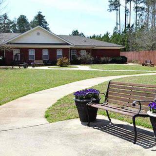 A peaceful garden setting with a bench and a pathway leading to a brick building.