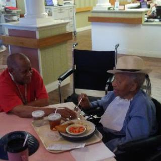 Two elderly individuals sharing a meal and enjoying each other's company in a care facility.